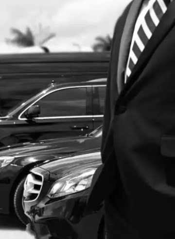 Chauffeur in a dark suit standing beside a row of black sedans