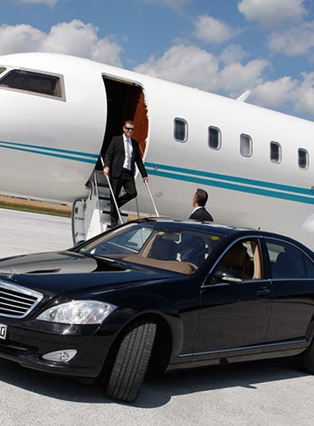 Chauffeur waiting by a black sedan as a traveler steps off a private jet